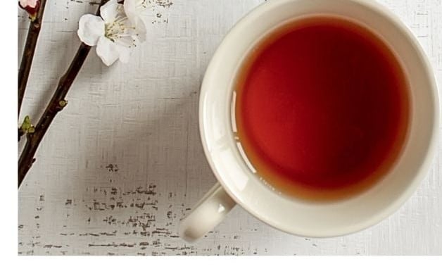 A white cup of Earl Grey tea beside a branch of white blossoms on a rustic white table.