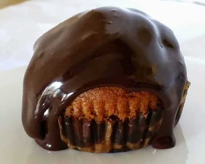 A pumpkin muffin covered in glossy chocolate glaze dripping down the paper liner.