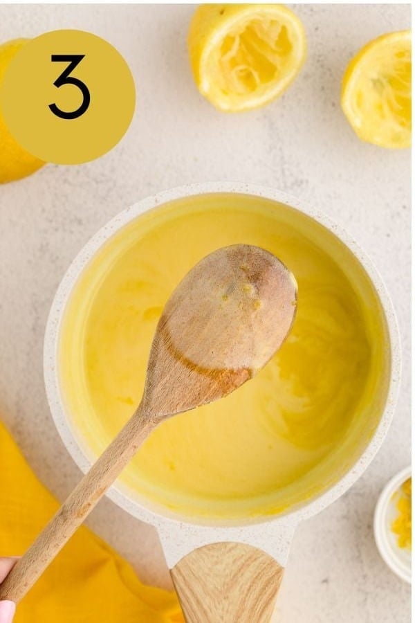 Thickened lemon curd coating a wooden spoon in the saucepan.