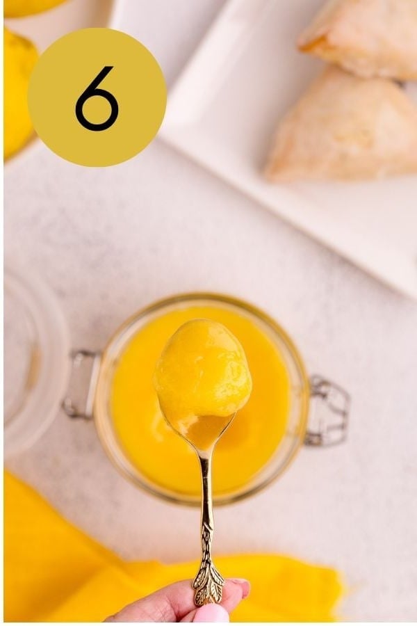 A spoonful of thick lemon curd lifted from a glass jar.