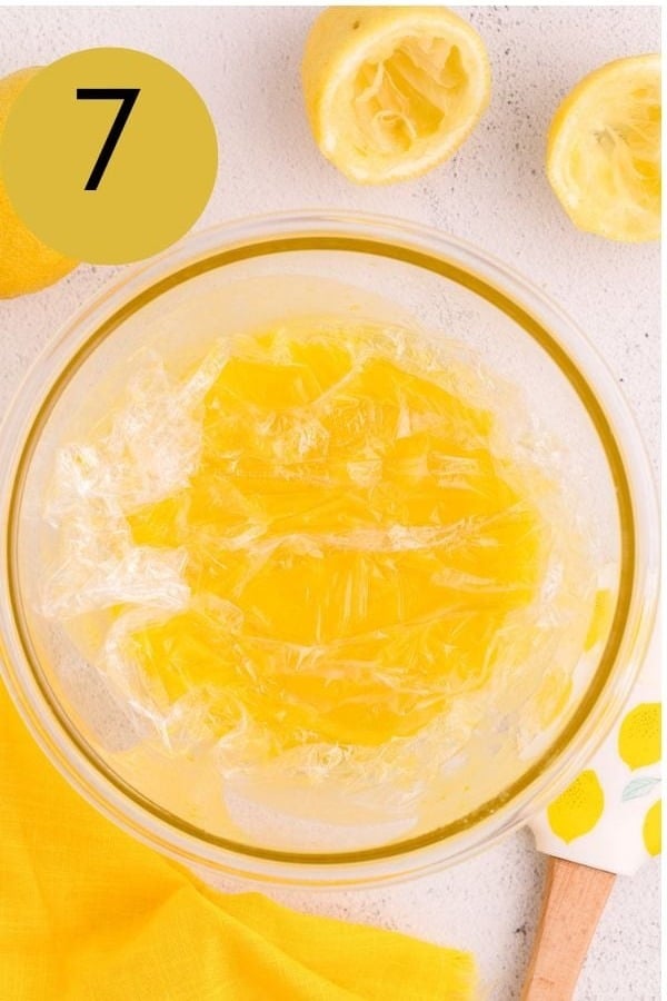 Plastic wrap pressed onto the surface of lemon curd in a glass bowl.