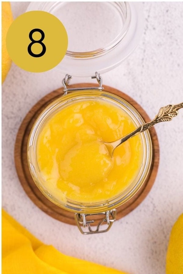 Finished lemon curd in a glass jar with a gold spoon.