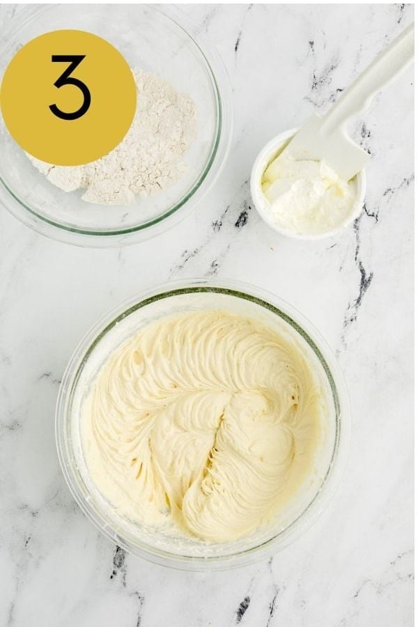 Creamy lemon cake batter in a bowl beside the dry ingredients and sour cream.