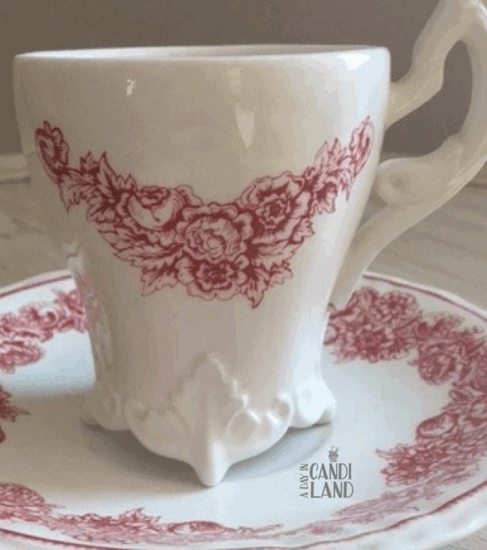 A white footed teacup with red rose trim on a matching saucer.